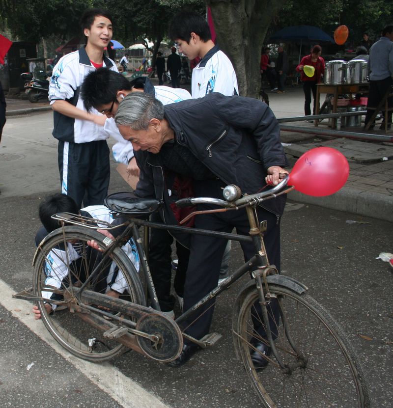 (学生们帮老爷爷的自行车打气)